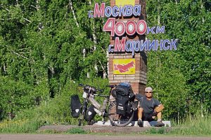 Foto zu Diashow "Der Sonne entgegen - Wladiwostok", Reiseimpressionen von Thomas Meixner. Zu sehen sind der Autor mit Fahrrad vor einem gemauerten Wegweiser mit dem Hinweiß "4000 Km von Mariinsk nach Moskau".